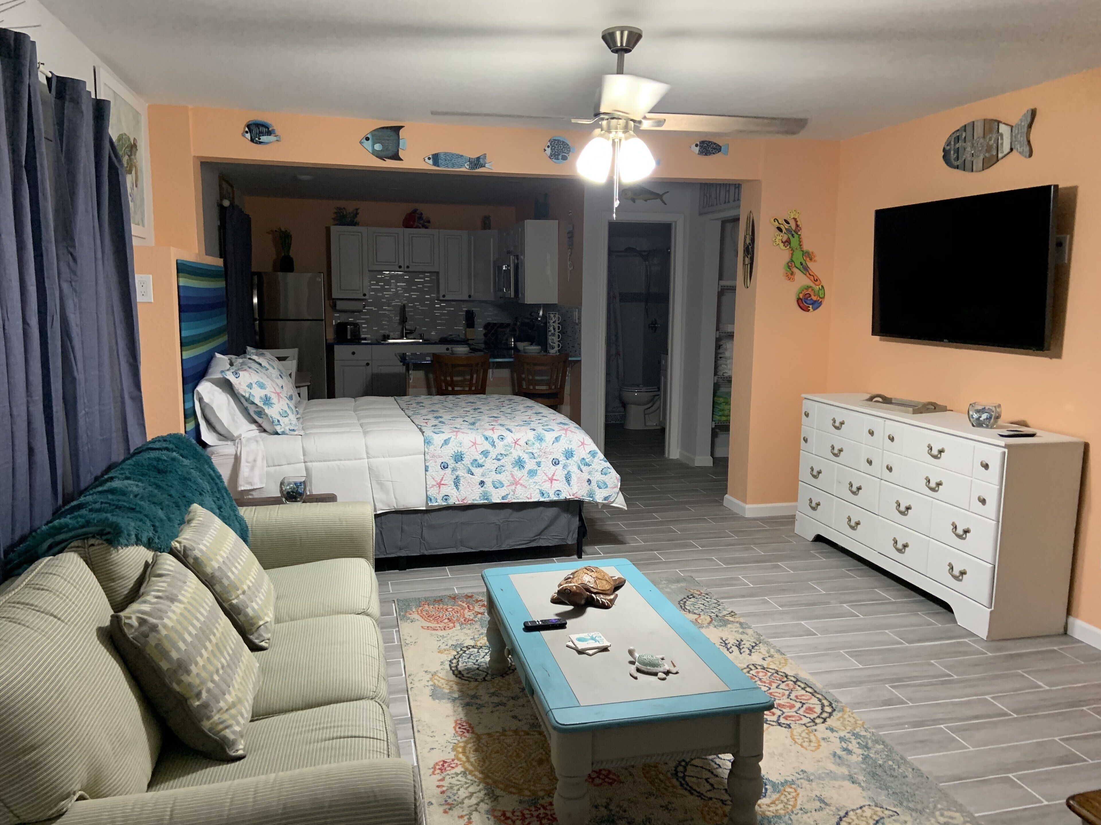 Un espacio habitable compacto con sofá, una mesita de centro, televisor y kitchenette.