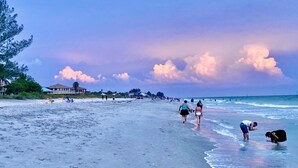 Une plage où l’on voit des gens se promener et nager, une maison en arrière-plan et un ciel dégagé.