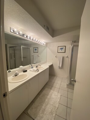 Ein Badezimmer mit zwei Waschbecken, einem großen Spiegel mit Beleuchtung, einer Dusche und einem flauschigen Teppich.