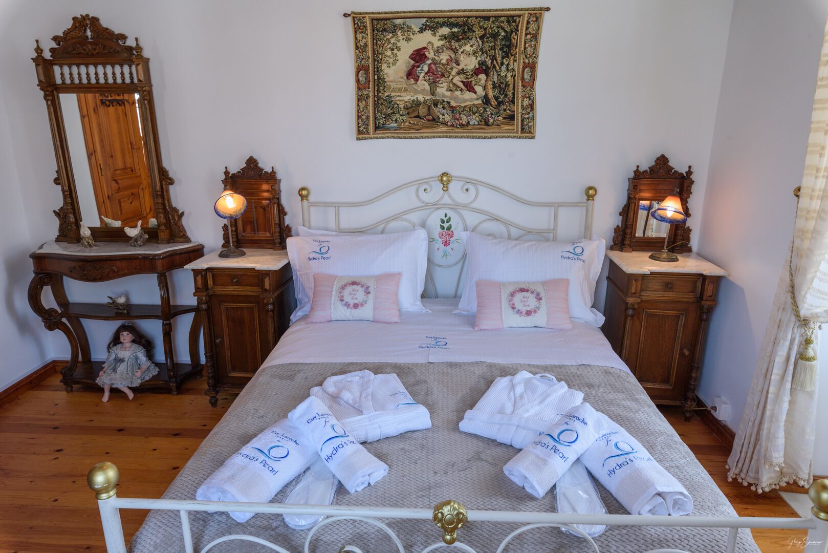 A neatly arranged bedroom with a bed, two bedside tables, a dresser, a mirror, and a painting on the wall.