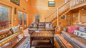 A wooden cabin interior with a sofa, a coffee table, and a staircase. - Booking Summer! 4 Masters Family Friendly Hot Tub Fire Pit Secluded Yard (Sevierville)