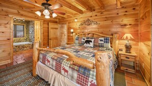 A log cabin bedroom with a wooden ceiling, a bed with a plaid quilt, a wooden headboard, a nightstand, and a lamp. - Booking Summer! 4 Masters Family Friendly Hot Tub Fire Pit Secluded Yard (Sevierville)