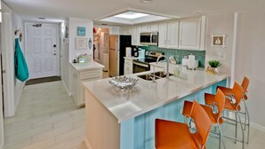 A modern kitchen with white cabinets, a central island with bar stools, a microwave, and a refrigerator. - Modern Oceanfront condo for your Beach Getaway! Spectacular views! (South Padre Island)
