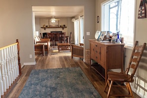 A spacious living area with a wooden floor, a blue rug, a dining table, and a wooden cabinet with a chair.