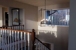 A staircase with white balusters and a wooden handrail, a hanging light fixture, and a framed map on the wall.