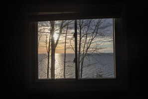 Ein Fenster mit Blick auf Bäume und ein Gewässer bei Sonnenuntergang.