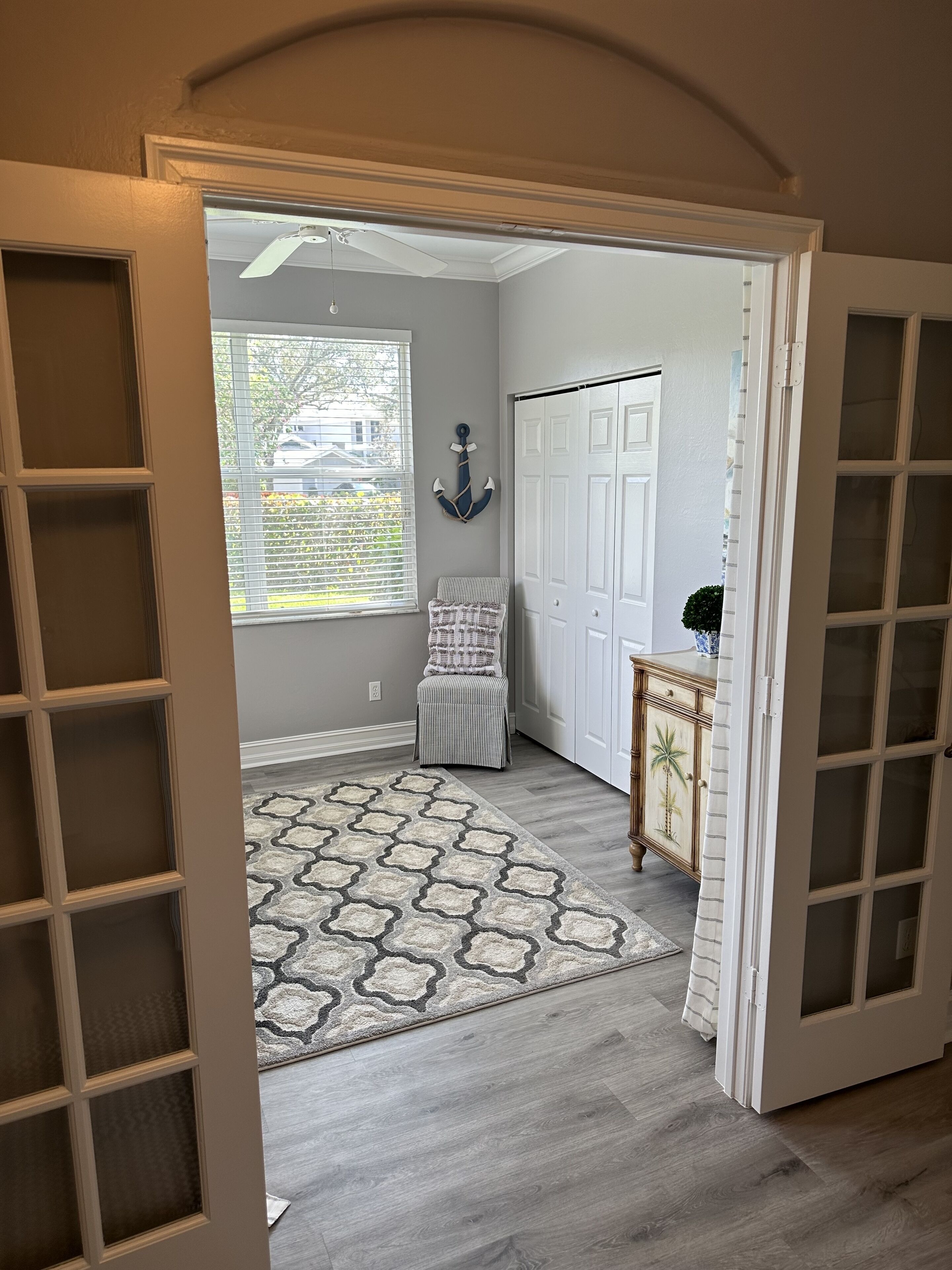 A hallway with a patterned rug, a chair, a decorative wall anchor, and a cabinet with a palm tree design.