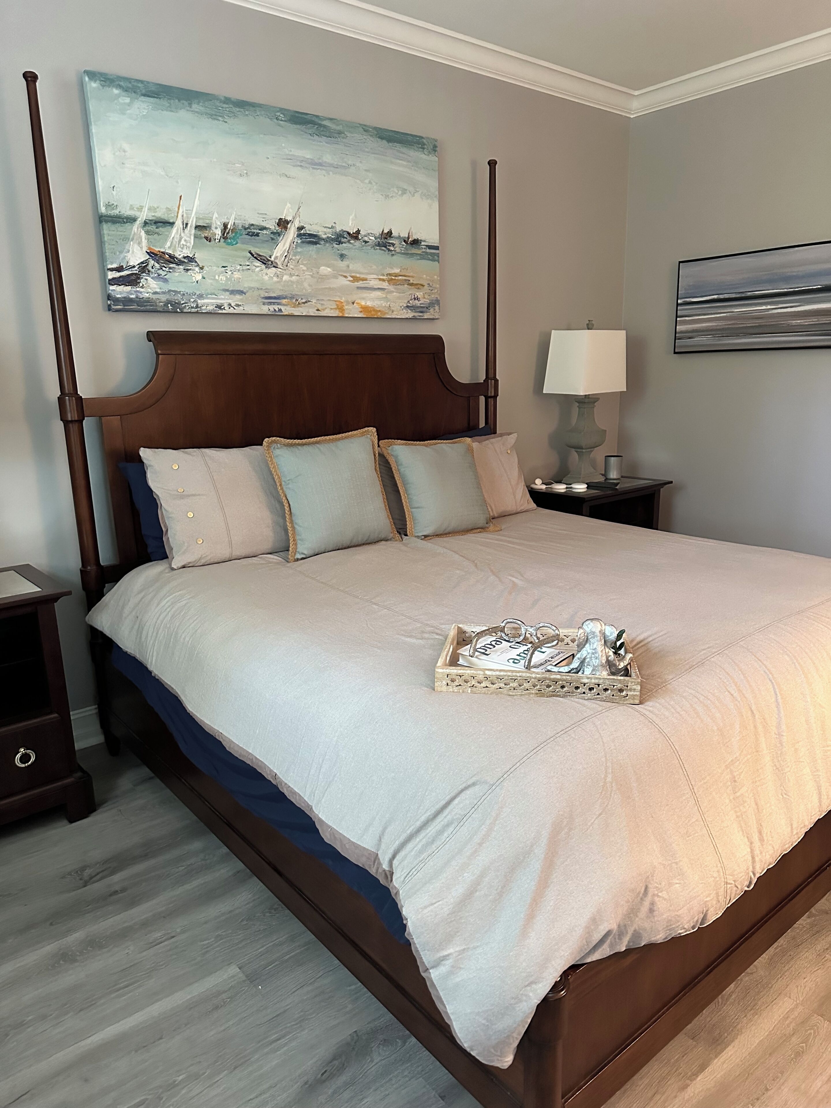 Een hemelbed met houten hoofdbord, een beige sprei, en een dienblad met sleutels en sleutelhanger op het bed.