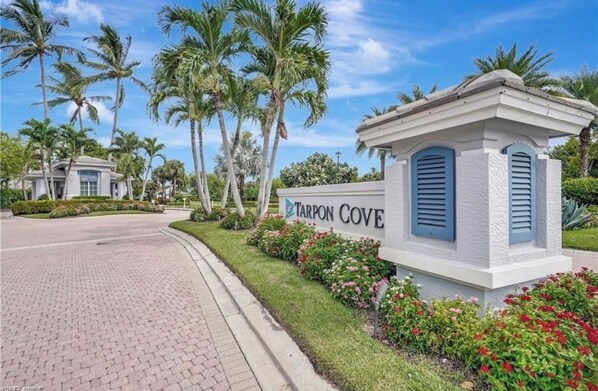 A sign for Tarpon Cove with a paved road and palm trees in the background.