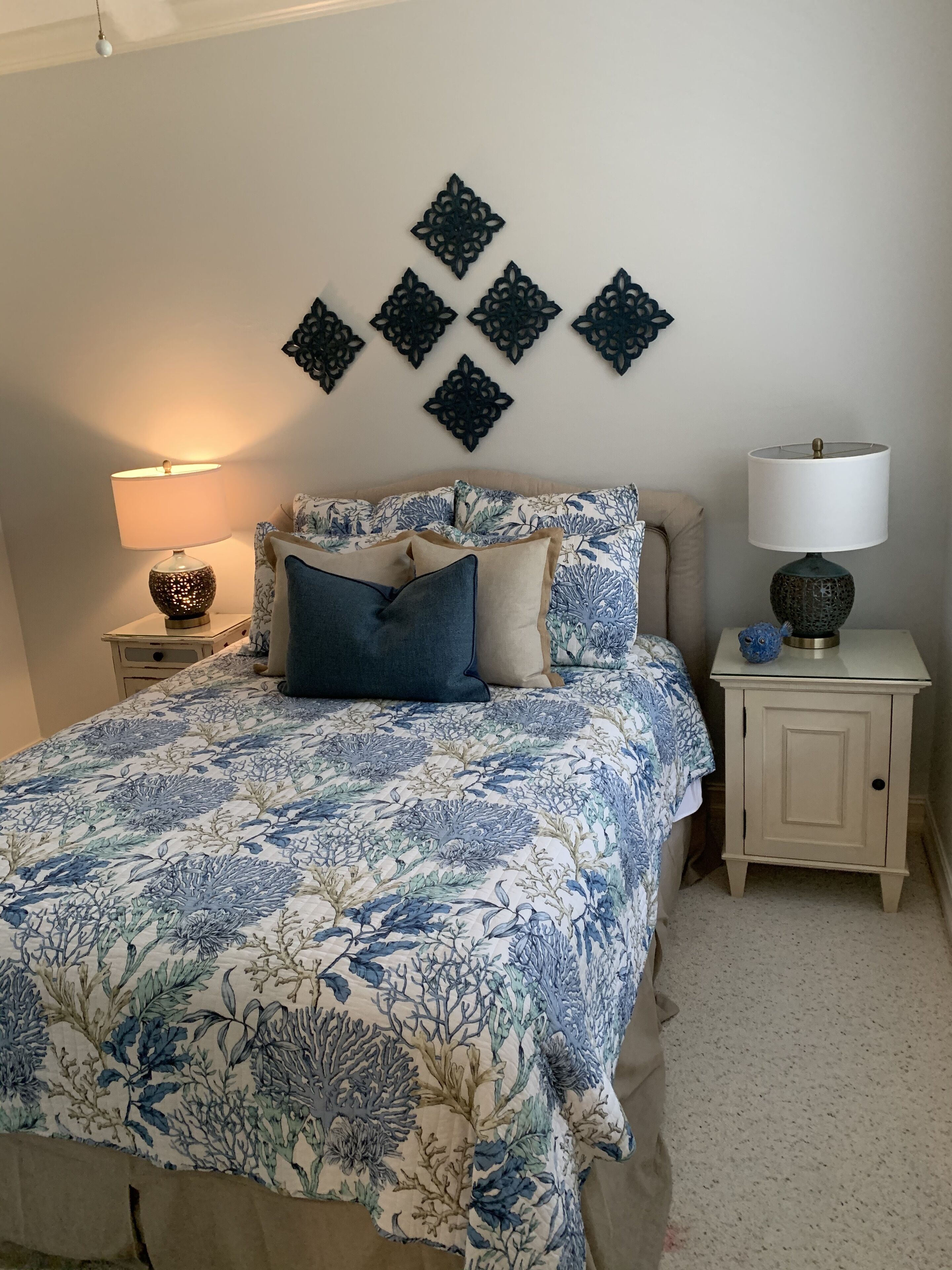 Une chambre à coucher avec une couvre-lit à motifs floraux, deux lampes de chevet, des œuvres d’art décoratives au mur et une table de chevet sur laquelle est posé un vase.