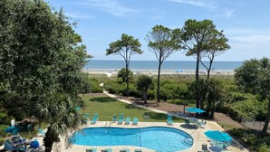 Una piscina amb gandules i ombrel·les, envoltada de vegetació i vista a la platja.