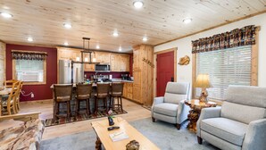 Un salón acogedor con chimenea, un comedor con sillas de madera y una cocina con armarios de madera y electrodomésticos modernos.