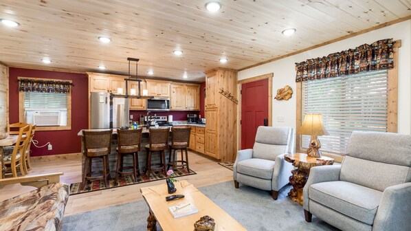 A cozy living room with a fireplace, a dining area with wooden chairs, and a kitchen with wooden cabinets and modern appliances.