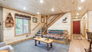 Interior acogedor de una cabaña con una escalera de madera, un sofá con motivos de 'Yellowstone', una mesa de centro y una ventana con persianas.