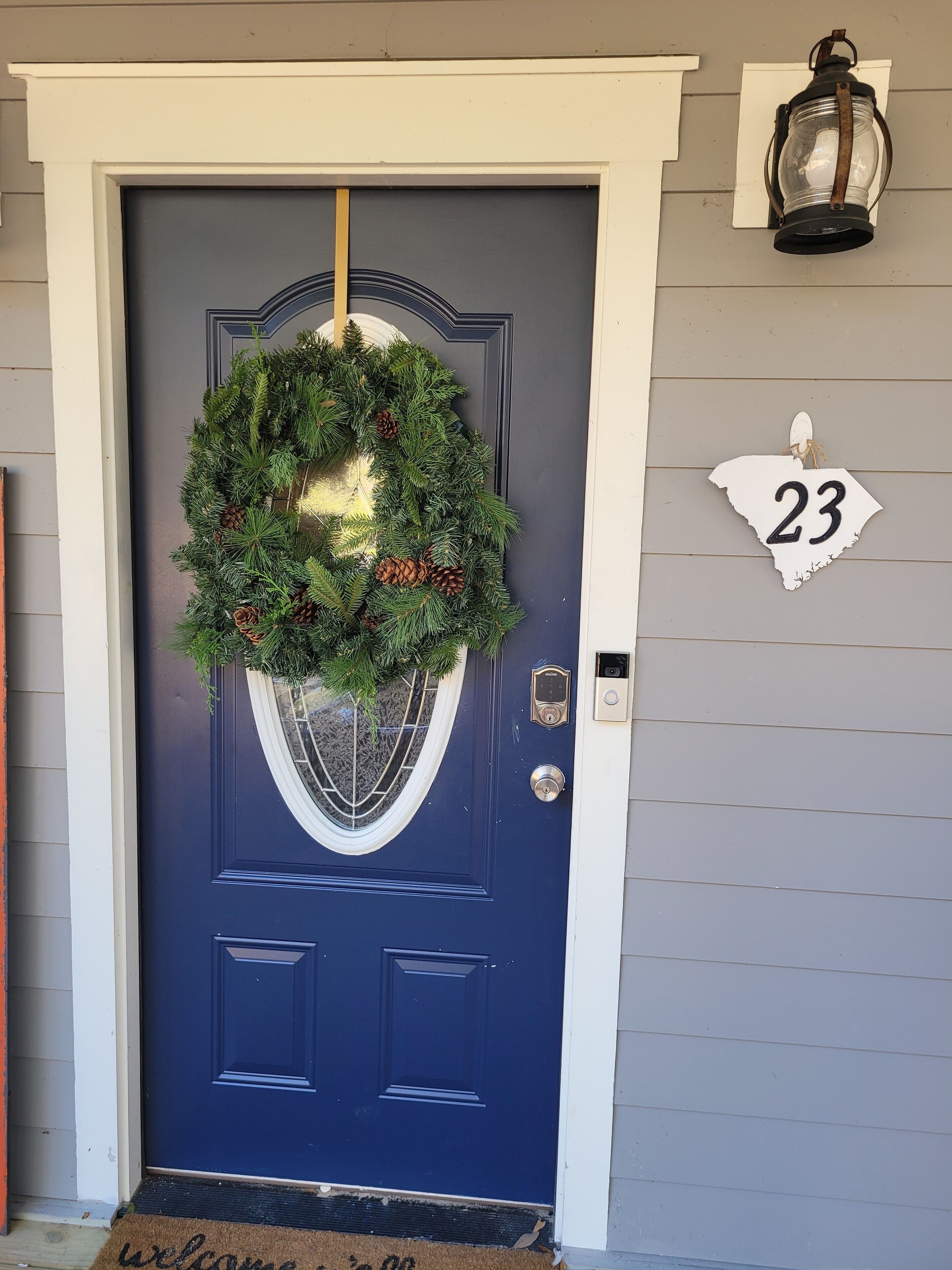 A dark blue door with a wreath, a house number sign, and a doorbell.