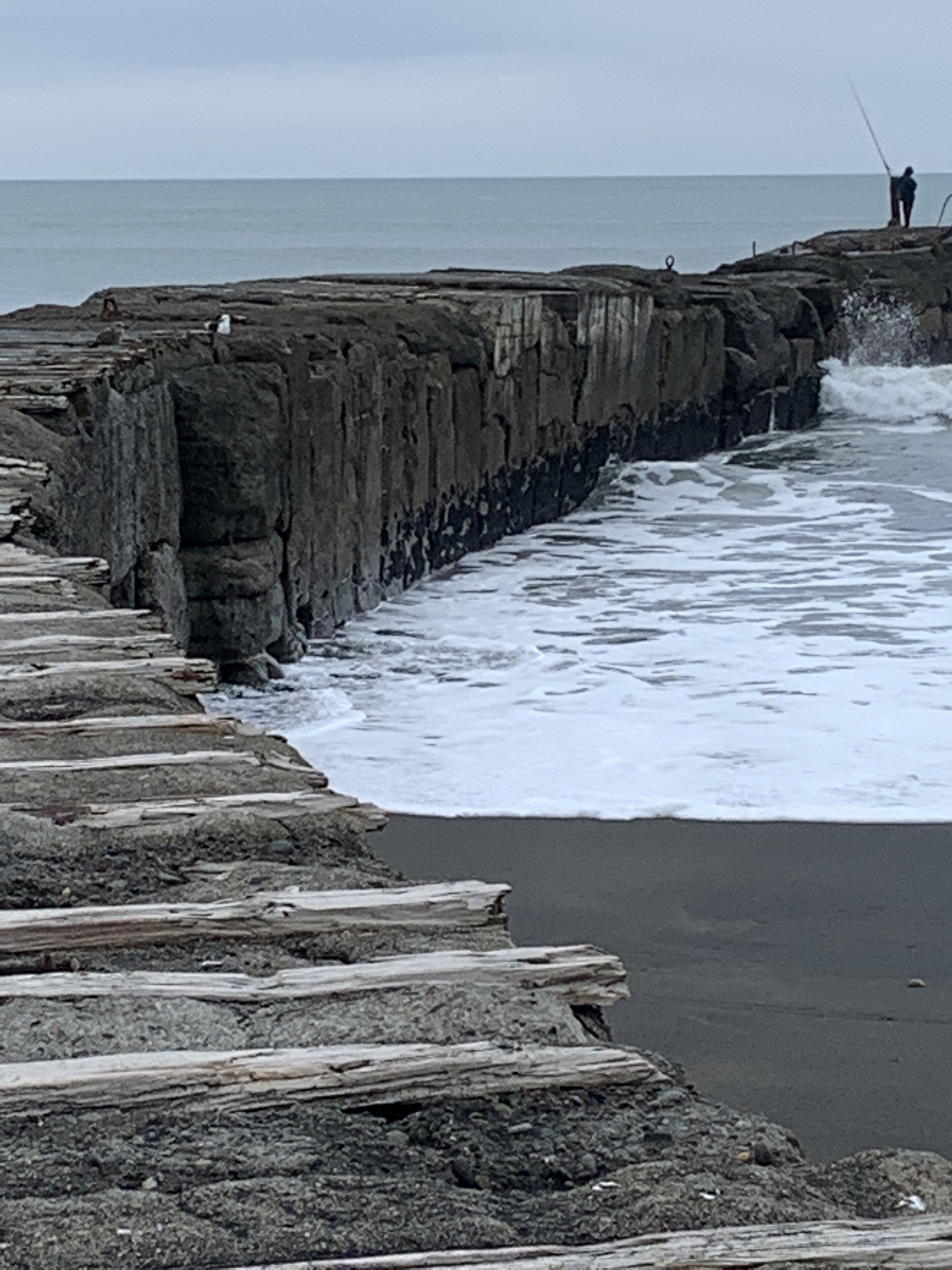 A rocky pier extending into the sea with waves crashing against it.