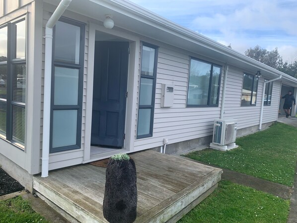 A single-story mobile home with a front porch, a small garden, and a clear sky.