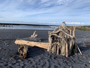 A beach with driftwood and a pier in the background.