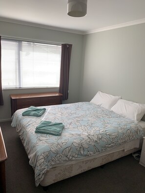 A bedroom with a bed, a nightstand, a window with curtains, and a bench.
