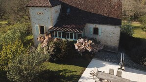 A stone building with a tiled roof, a small balcony, and a garden area with a table and chairs. - Character house with swimming pool between Lot and Dordogne (Gourdon)
