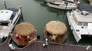 Eine Anlegestelle mit zwei strohgedeckten Gebäuden, einem weißen Boot mit Kabine und einem weiteren Boot mit Überdachung.
