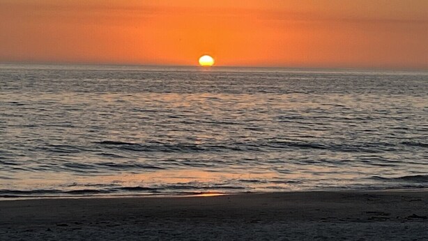 Ein Sonnenuntergang über einem ruhigen Meer mit einem Strand im Vordergrund.