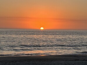 Un coucher de soleil sur une mer calme, avec une plage au premier plan.