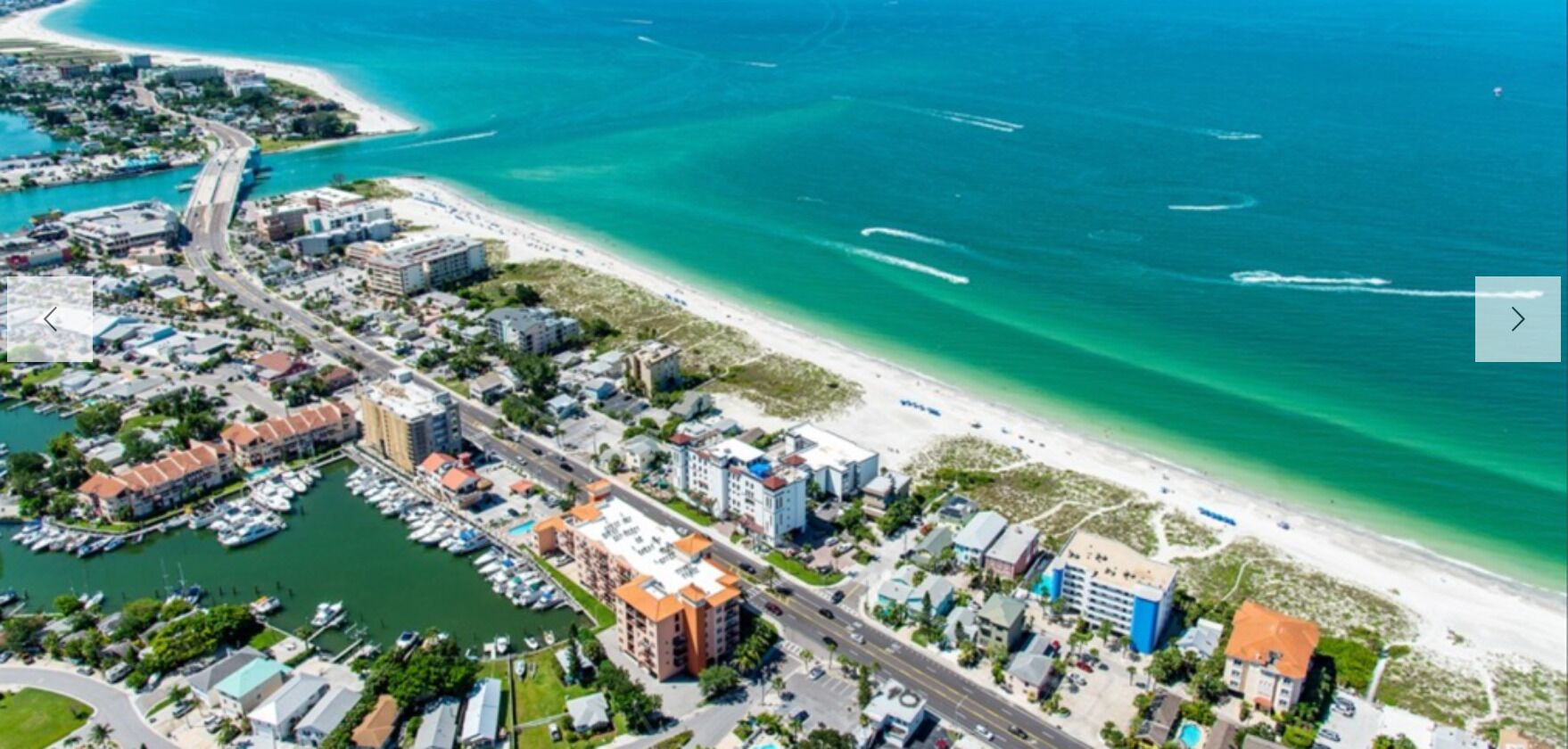 An aerial view of a coastal town with a marina, buildings, and a beach.