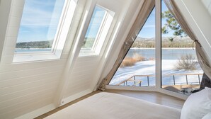 Una camera da letto con un'ampia finestra che si affaccia su un paesaggio innevato e un lago.