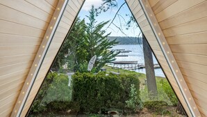 Una stanza accogliente con una finestra triangolare che dà sul lago, pareti in legno e due cuscini confortevoli.