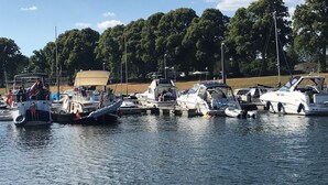 Un puerto deportivo con varias embarcaciones amarradas, rodeado de árboles y cielos despejados.
