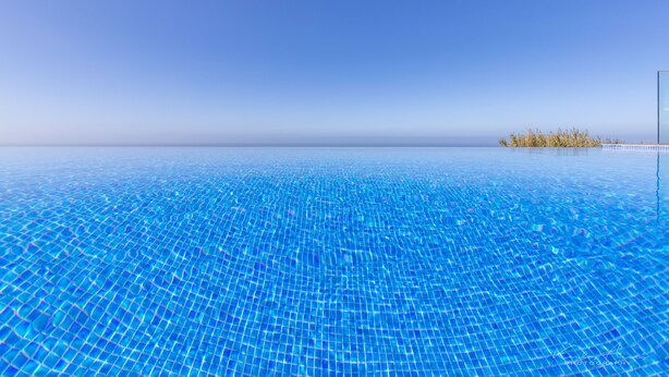 Une piscine d’eau cristalline, d’un bleu profond, qui offre une vue sur l’horizon et sur une petite île au loin.