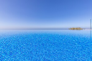 A clear blue pool with a view of the horizon and a small island in the distance.