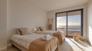 Une chambre moderne avec deux lits, une grande porte-fenêtre coulissante donnant sur la plage et une échelle en bois.