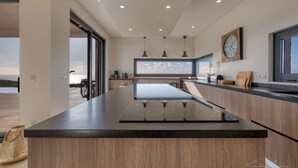 Une cuisine moderne dotée d’un grand îlot central, de luminaires suspendus et d’une grande fenêtre donnant sur l’océan.