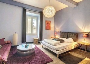 Relax in this serene bedroom with a large bed, round coffee table, and a unique chandelier.