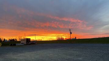 A rural landscape with a sunset, open fields, and a trailer.