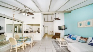 A spacious living area with a glass dining table, cushioned chairs, a white sofa, and a ceiling fan. - Beachfront Resort Condo, Walk to Atlantis (Paradise Island)
