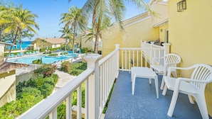 A balcony with white chairs, a pool, and palm trees. - Beachfront Resort Condo, Walk to Atlantis (Paradise Island)
