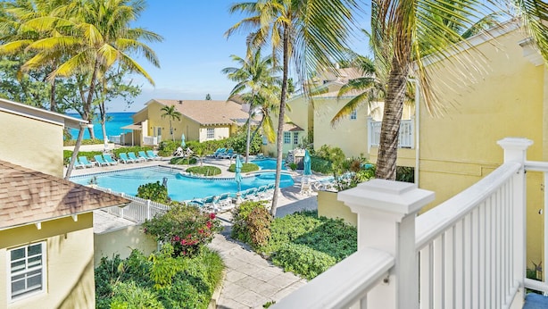 A pool area with lounge chairs and palm trees, surrounded by buildings with a yellow facade. - Beachfront Resort Condo, Walk to Atlantis (Paradise Island)