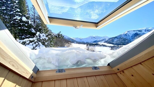 A wooden hot tub with a skylight overlooking a snowy mountain landscape.