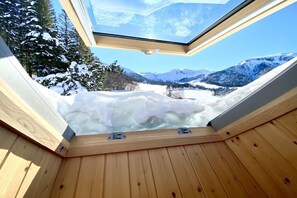 Un jacuzzi de madera con tragaluz que da a un paisaje montañoso nevado.