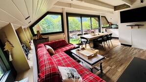 A modern interior with a red plaid sofa, a dining table, and a kitchen area.