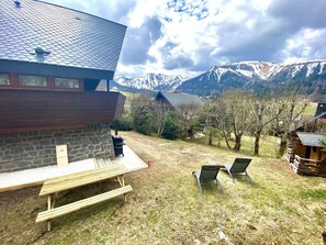 A stone building with a sloped roof, a wooden bench, and two metal chairs in a grassy yard with a mountain view. - Chalet " LA JANELLE " Le Mont-Dore (Mont-Dore)