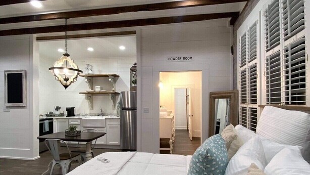 A modern bedroom with a large bed, a dining area, and a kitchen visible through an open door. - Charming Loft (Nashville)
