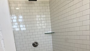 A shower with white hexagonal tiles and a glass shelf. - Charming Loft (Nashville)