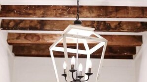 A hexagonal chandelier with multiple candle-like lights hanging from a chain, suspended from a wooden ceiling with exposed beams. - Charming Loft (Nashville)