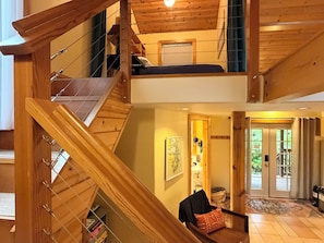 Una escalera de madera de varios niveles con una cama en el segundo piso y vistas al exterior.