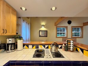 Una cocina con armarios de madera, estufa integrada, hervidor y una ventana con cortinas.