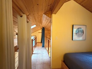 Un pasillo estrecho con vigas de madera en el techo, una cama con colchón y un cuadro en la pared.